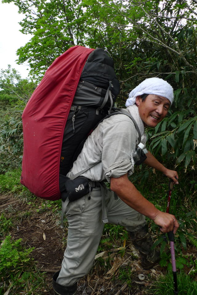 四輪駆動ですよ、と両手に杖の恰好で軽々と月山筍４０㌔を背負う真室川の姉崎さん（７月７日）